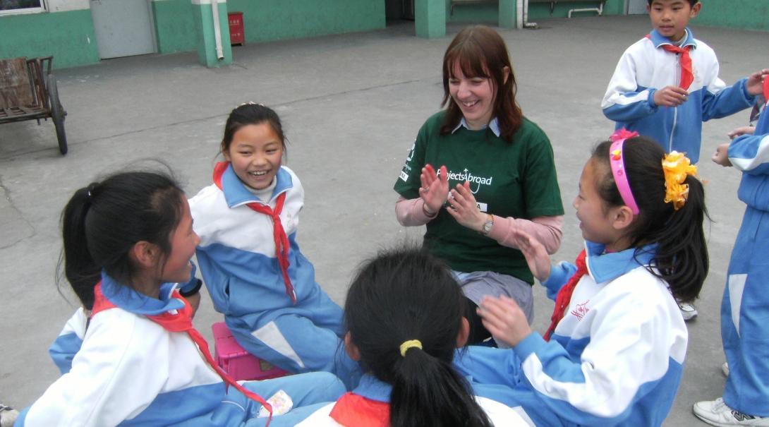 Female volunteer celebrates National Volunteer Week with children during her Childcare Project in China. Projects Abroad volunteer with children in China claps with children outside her kindergarten placement.